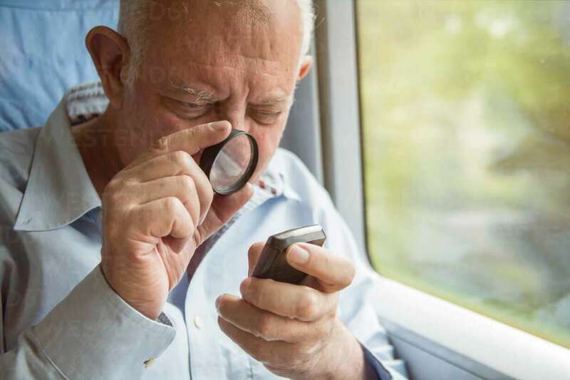 senior-man-reading-text-on-a-cell-phone-with-a-magnifying-glass-TAMF000123.jpg